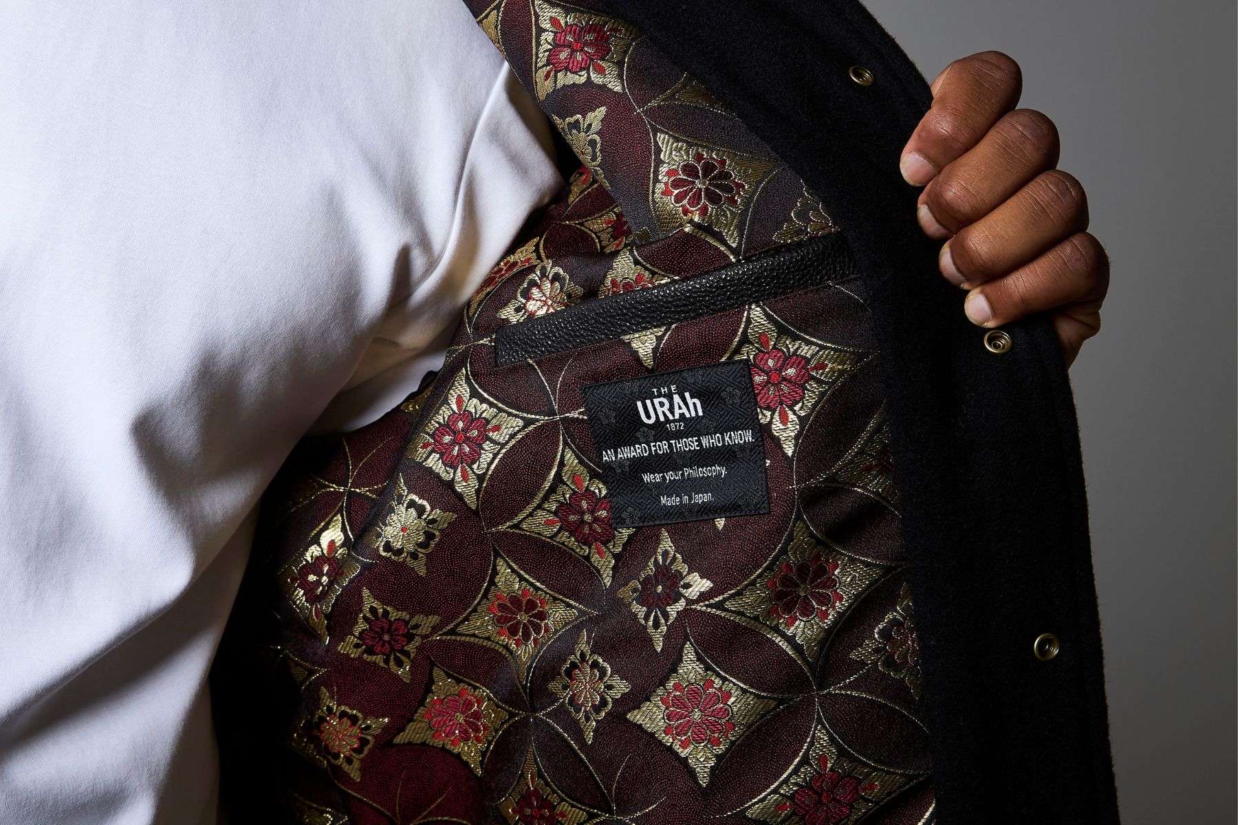 The jacket held open on the concept tag sewn into the inside pocket, against the crimson and gold lining.