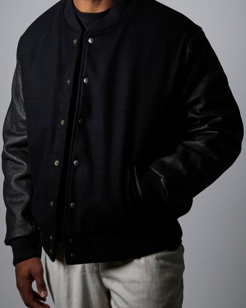 A black varsity jacket in Bishu melton wool, with sleeves in urushi-lacquered kurozan leather. Ribbing in black. Worn closed.