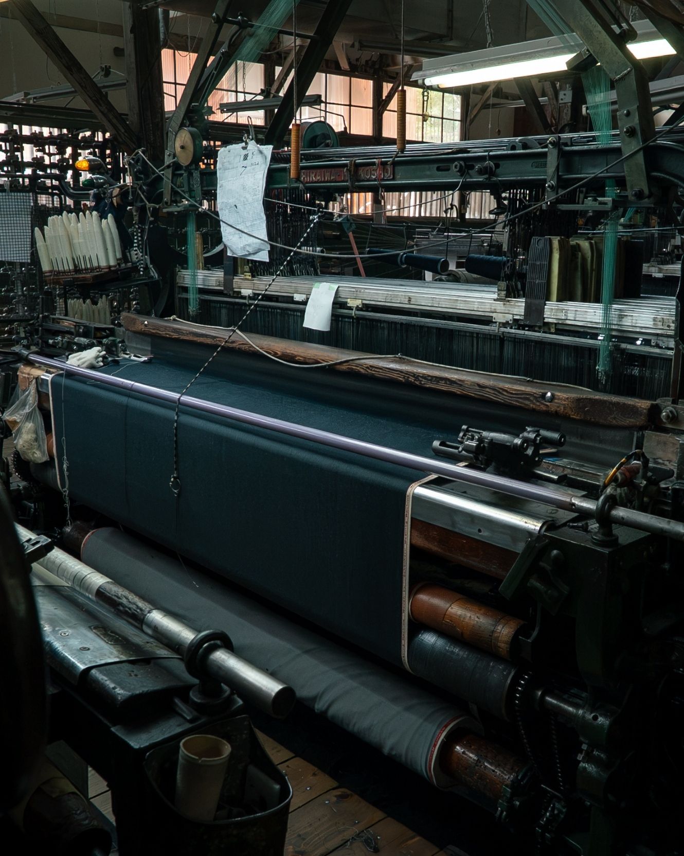 A loom in a darkened Bishu mill, black melton wool running through it.