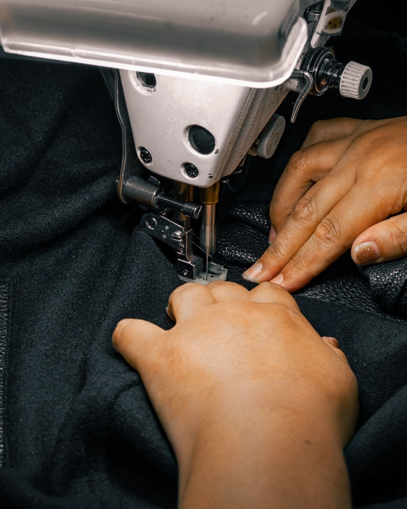 Two hands feeding black cloth beneath a sewing machine needle in Hanyu.