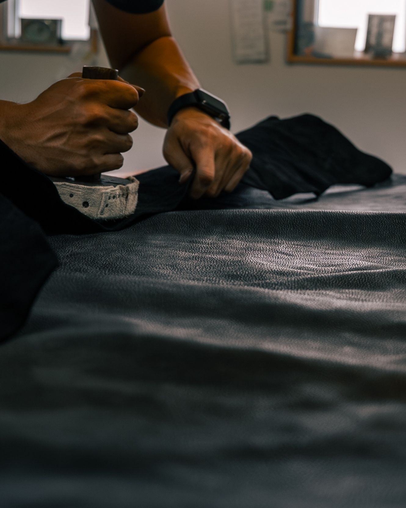 A craftsman’s hands working a tool across a sheet of kurozan leather in Himeji.