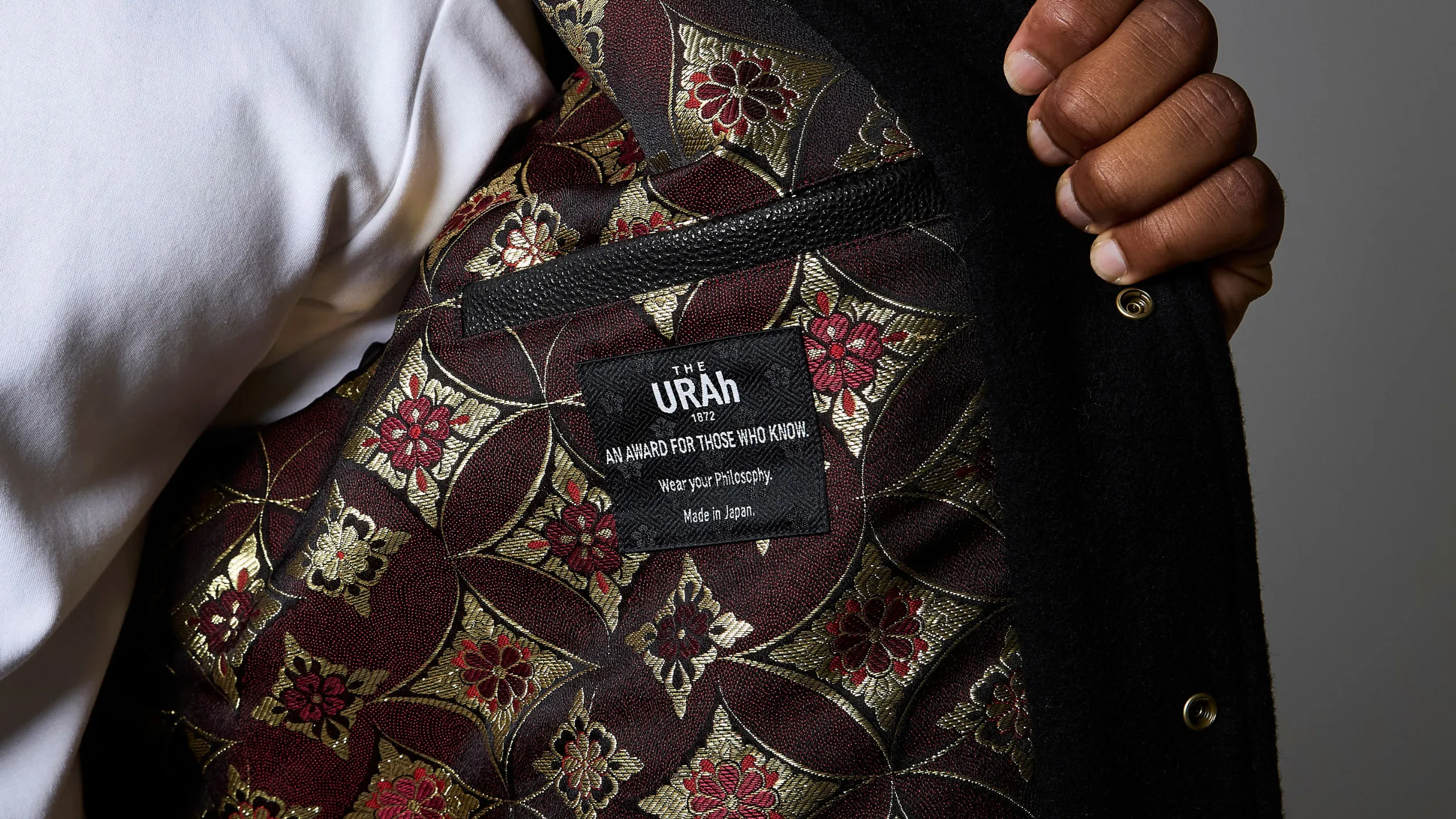 The jacket held open, showing the Kyo-ori jacquard lining in deep crimson and gold, with the woven brand label at the inside chest.